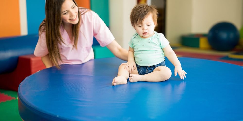 Cute female therapist helping a baby practice balance on an early stimulation and development school