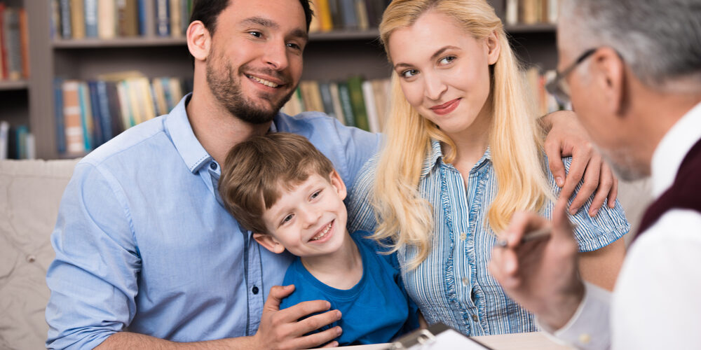 Happy family of three talking with psychologist. Psychologist taking notes. There are many books in psychologist office